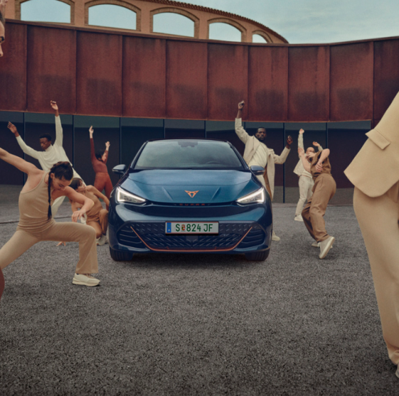 Beige gekleidete Tänzer tanzen um einen blauen Cupra Born herum