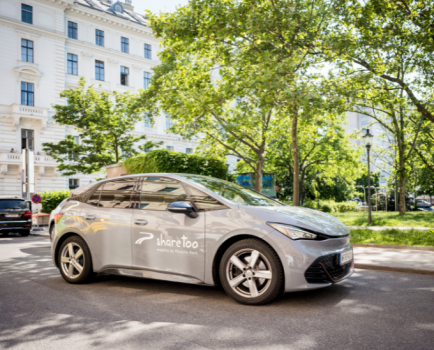 graues E-Auto auf einer Straße vor grünen Bäumen