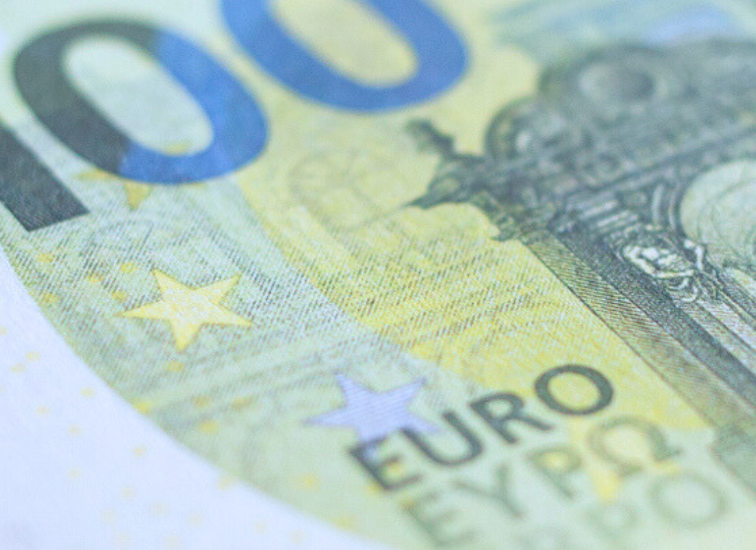 Makroaufnahme eines 100-Euro-Scheins mit Fokus auf den Schriftzug 'EURO' und den gelben Sternen, die das Design ergänzen.